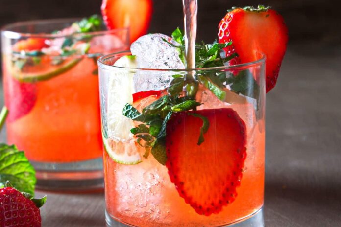 A refreshing strawberry mocktail served in a tall glass, garnished with a slice of fresh strawberry on the rim. The vibrant red drink is filled with crushed ice and adorned with a mint sprig for a burst of color and flavor.