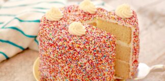 A delicious homemade cake topped with creamy frosting and colorful sprinkles, presented on a white cake stand.