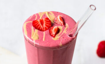 A refreshing strawberry smoothie served in a clear glass with a garnish of fresh strawberries on the rim.
