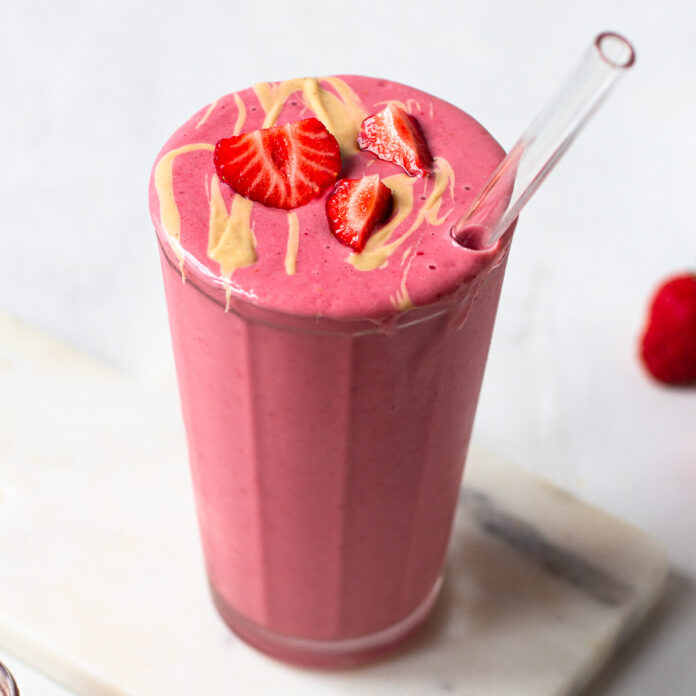 A refreshing strawberry smoothie served in a clear glass with a garnish of fresh strawberries on the rim.