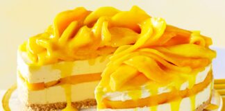 A vibrant mango cheesecake topped with fresh mango slices, served in a glass dish. The creamy dessert is eggless and requires no baking, perfect for summer indulgence.