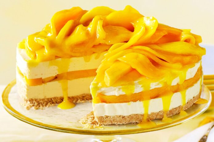 A vibrant mango cheesecake topped with fresh mango slices, served in a glass dish. The creamy dessert is eggless and requires no baking, perfect for summer indulgence.